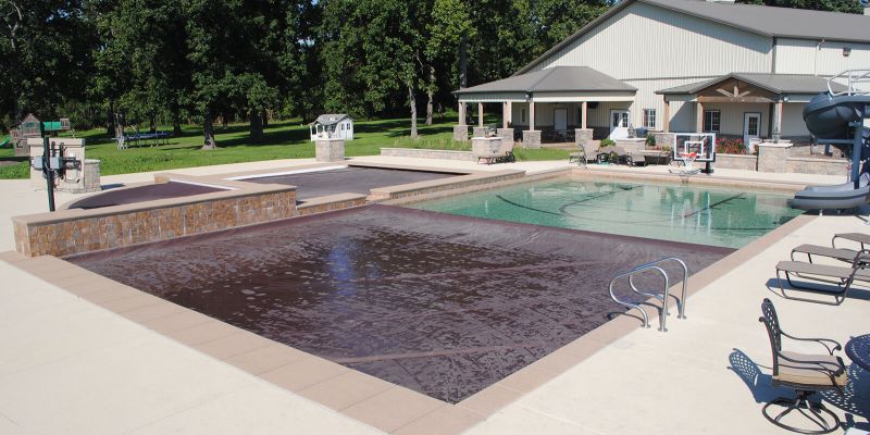 An in ground pool halfway covered by an automatic pool cover on a sunny day.