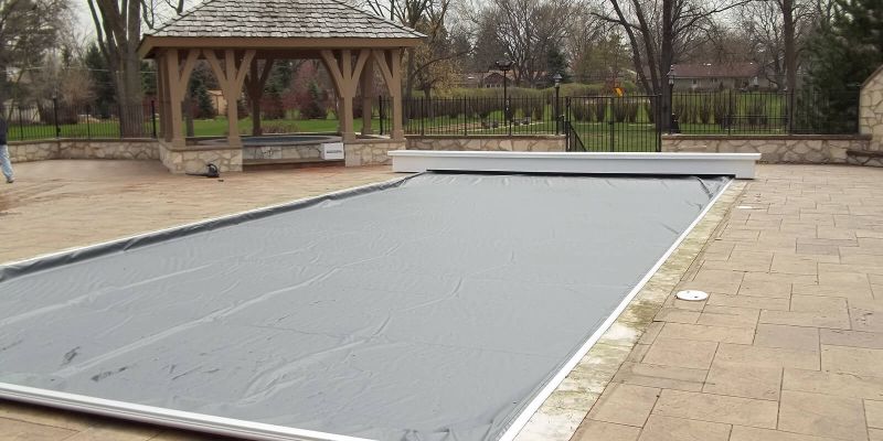 An in ground pool entirely covered by an automatic pool cover on a gloomy winter day.